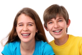A brother and sister with braces smile for the camera.
